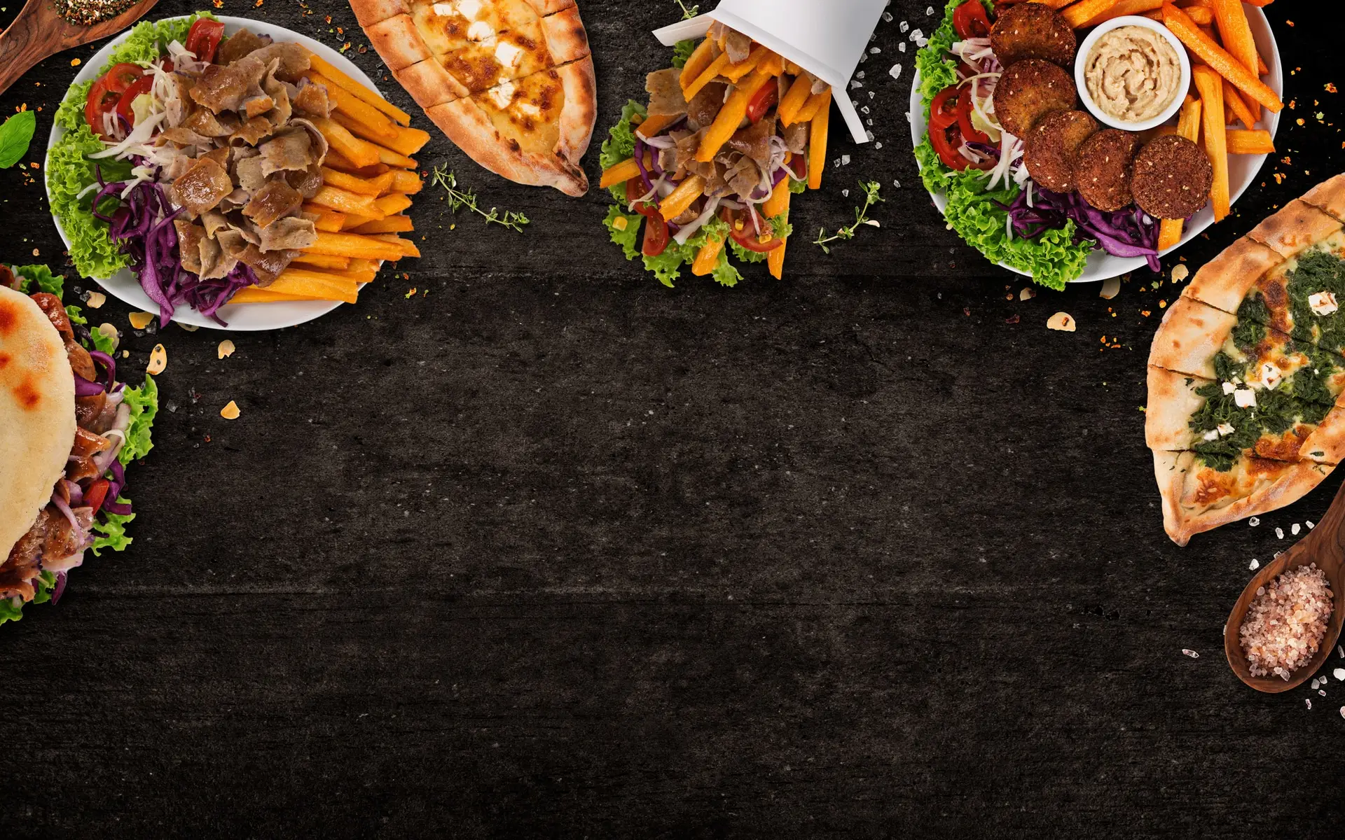 Von oben fotografiert: Kebabteller, Dürüm, Pide mit Spinat und Falafelteller auf dunklem Stein